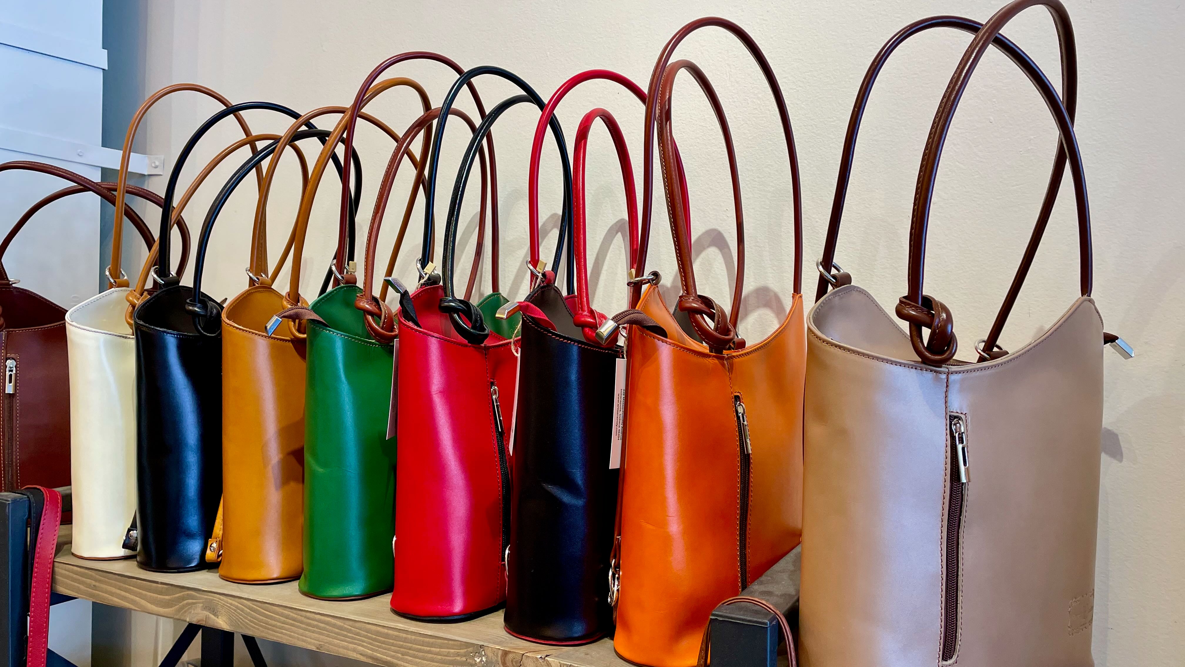 Row of colorful handbags on a wooden shelf against a white wall.