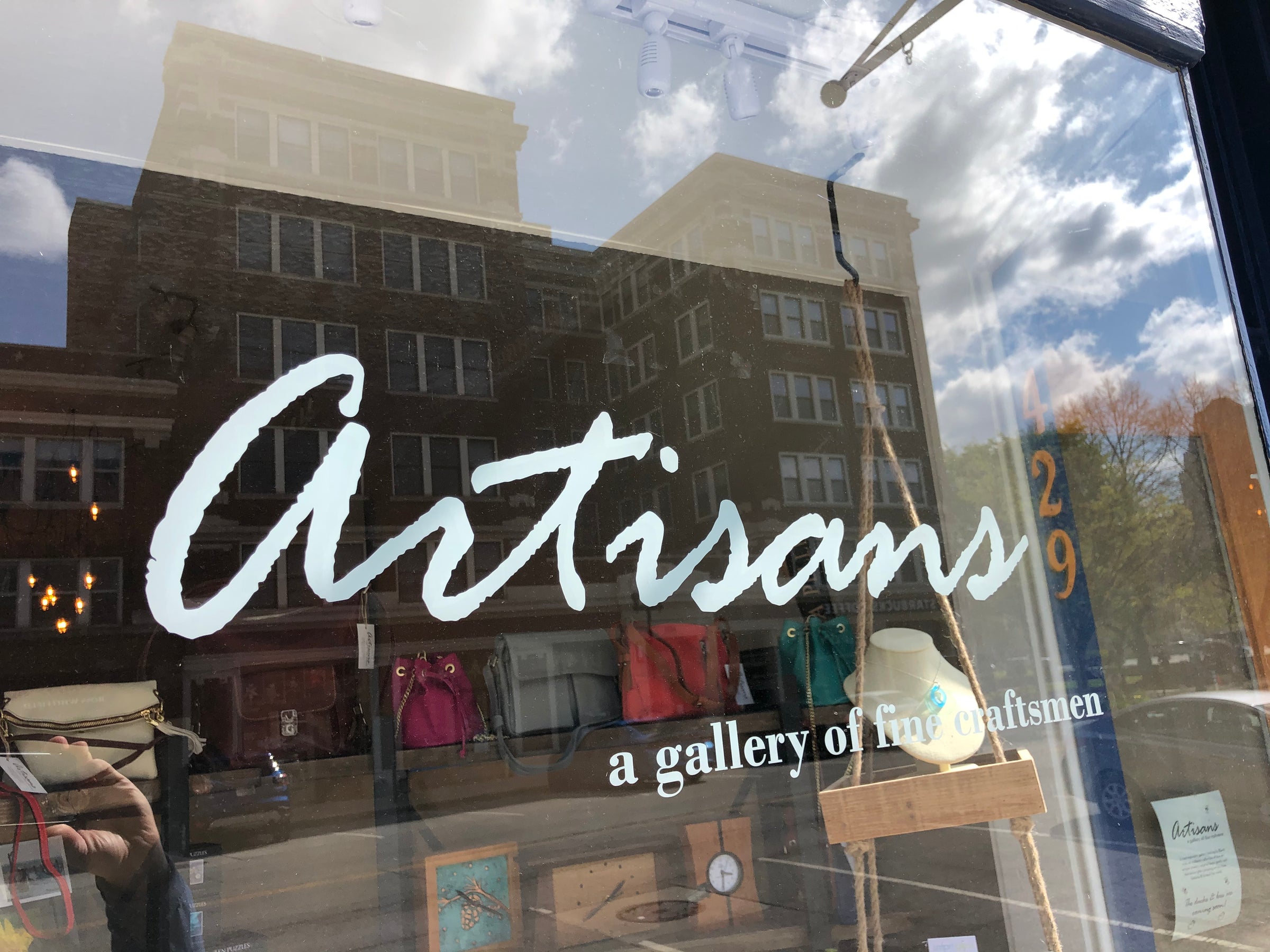 Storefront window with 'Artisans' sign and reflection of a building