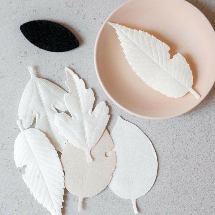 White leaf-shaped cookies on a gray surface with a pink plate.