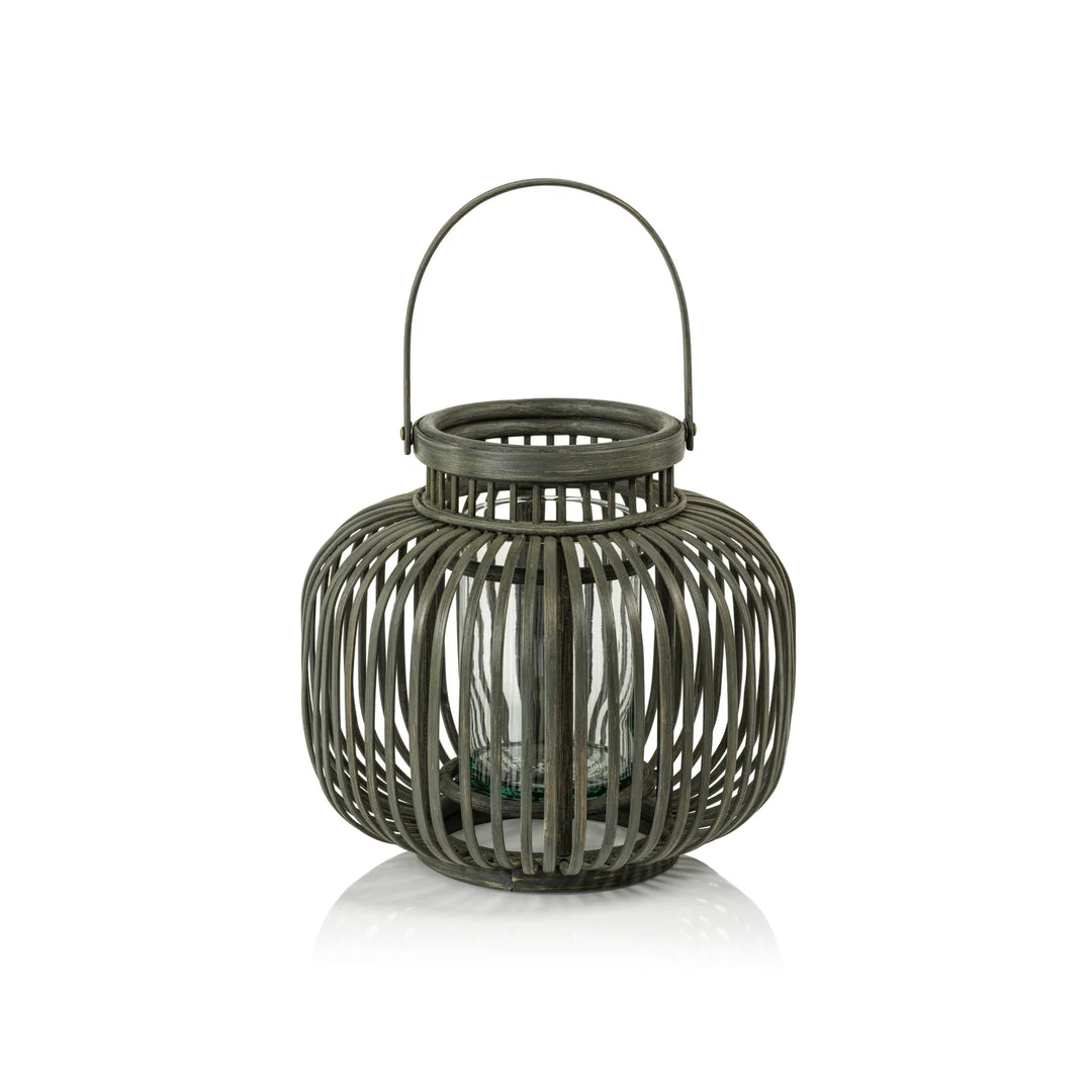 A dark gray metal lantern with a ribbed cylindrical body, a top handle, and a small glass candle holder inside, shown on a white background with a soft reflection | Artisans